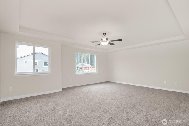 empty room with baseboards, a raised ceiling, carpet flooring, and a ceiling fan