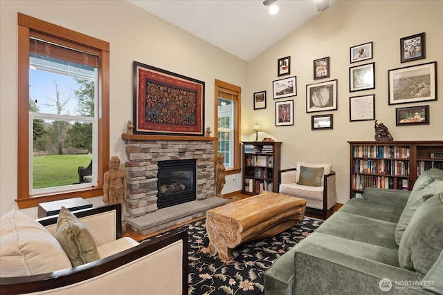 living room featuring a stone fireplace, vaulted ceiling, wood finished floors, and a wealth of natural light