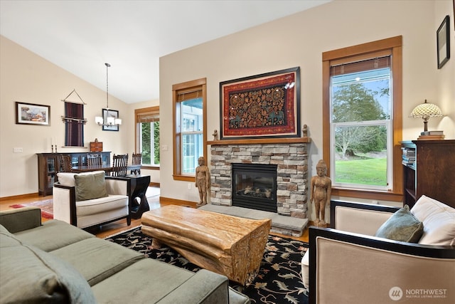 living area with lofted ceiling, wood finished floors, a stone fireplace, baseboards, and a chandelier