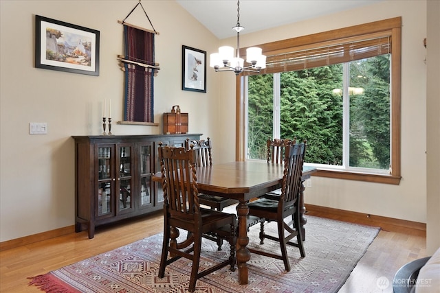 dining space featuring baseboards, light wood-type flooring, an inviting chandelier, and vaulted ceiling