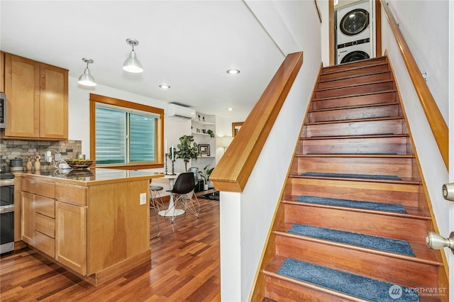 staircase featuring recessed lighting, stacked washer and clothes dryer, a wall mounted air conditioner, and wood finished floors