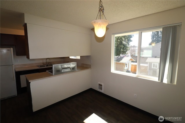 kitchen with dishwashing machine, a peninsula, freestanding refrigerator, a sink, and light countertops