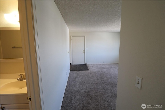 hallway with baseboards, a textured ceiling, carpet, and a sink