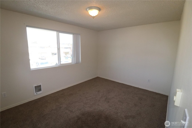 unfurnished room with dark colored carpet, visible vents, baseboards, and a textured ceiling