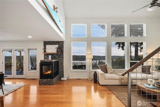 living area with french doors, a towering ceiling, wood finished floors, a glass covered fireplace, and a ceiling fan