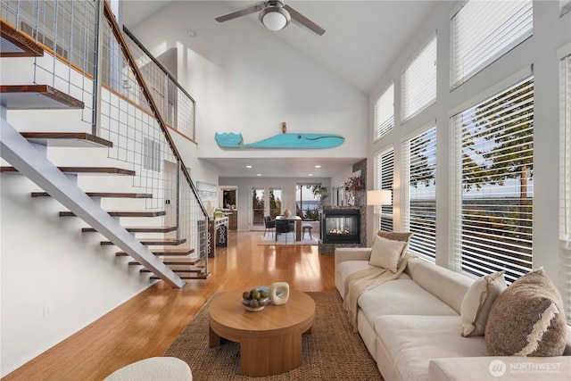 living area featuring stairway, wood finished floors, a multi sided fireplace, ceiling fan, and a towering ceiling