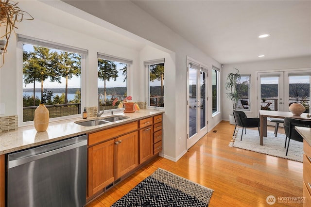 kitchen featuring brown cabinets, a sink, light stone counters, stainless steel dishwasher, and french doors