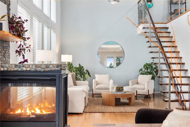 living room featuring wood finished floors, a high ceiling, a fireplace, and a healthy amount of sunlight