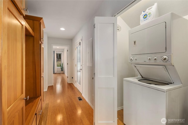 laundry area featuring light wood-type flooring, stacked washer / drying machine, baseboards, and laundry area