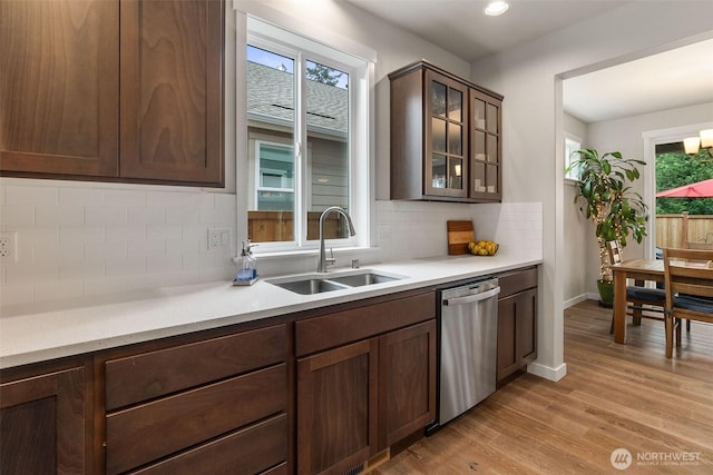 kitchen featuring glass insert cabinets, light countertops, light wood-style flooring, stainless steel dishwasher, and a sink