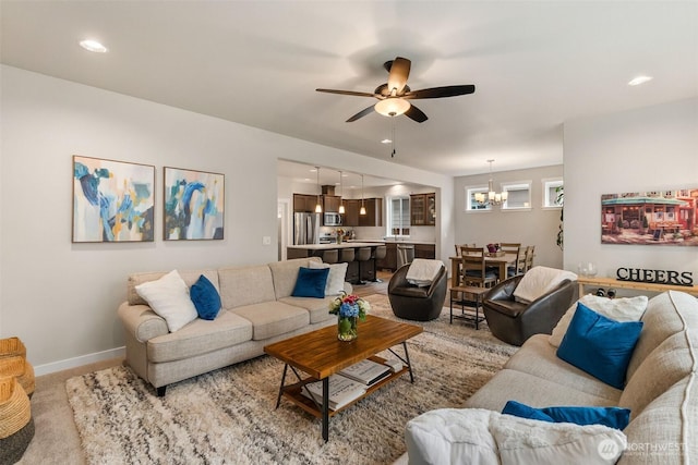 living room with recessed lighting, ceiling fan with notable chandelier, baseboards, and light carpet