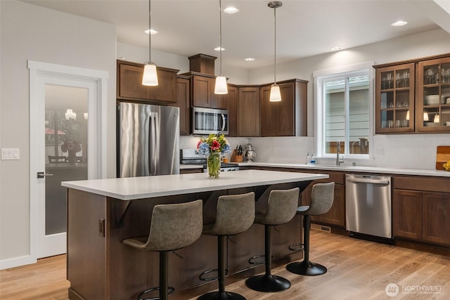 kitchen featuring a breakfast bar, light wood-style flooring, stainless steel appliances, decorative backsplash, and light countertops