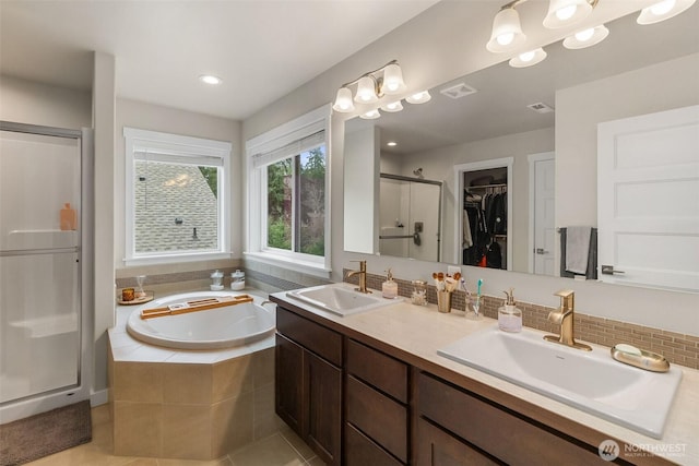 full bath with a walk in closet, a shower stall, a garden tub, and a sink