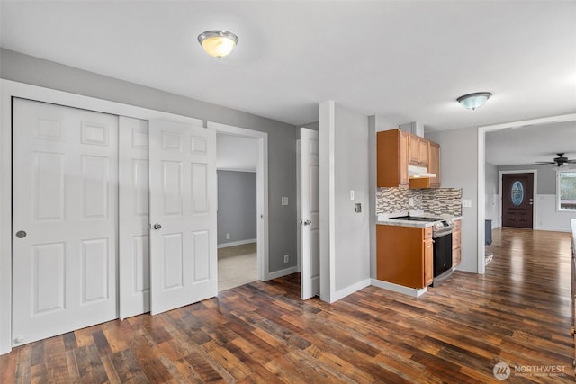 kitchen with stainless steel electric stove, dark wood-style flooring, decorative backsplash, light countertops, and under cabinet range hood