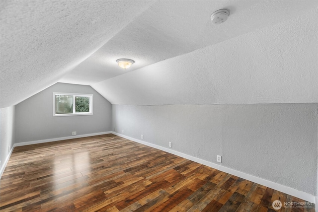 bonus room with vaulted ceiling, a textured ceiling, a textured wall, and hardwood / wood-style floors