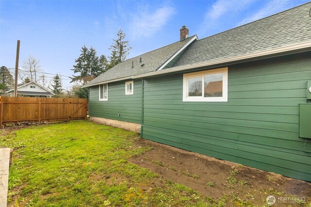 back of house with a shingled roof, a chimney, a yard, and fence