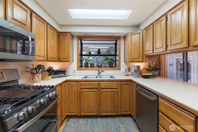 kitchen with brown cabinetry, appliances with stainless steel finishes, light countertops, and a sink