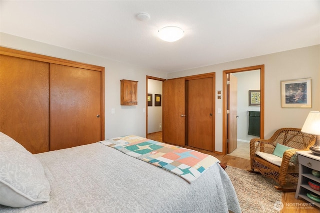 bedroom with ensuite bath, light wood-style flooring, and two closets