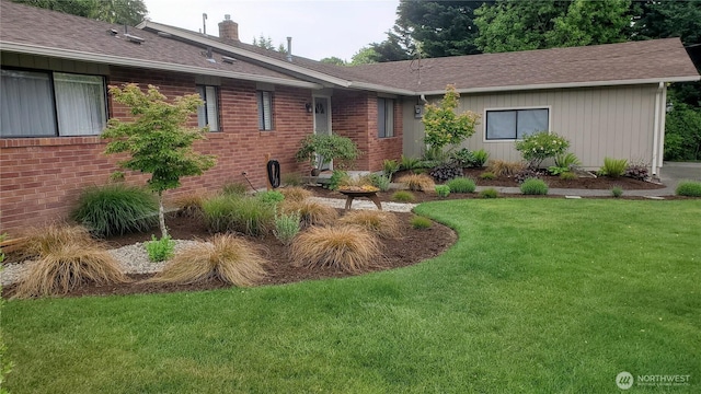 view of front of property featuring brick siding, a chimney, a front yard, and roof with shingles