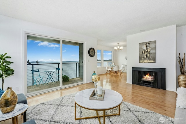 living area with a notable chandelier, wood finished floors, baseboards, and a lit fireplace