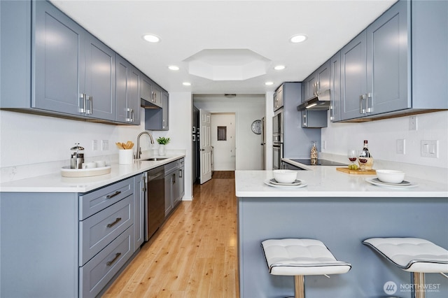 kitchen featuring a breakfast bar, a sink, under cabinet range hood, stainless steel appliances, and a peninsula