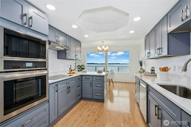 kitchen featuring under cabinet range hood, gray cabinets, a notable chandelier, stainless steel appliances, and a sink