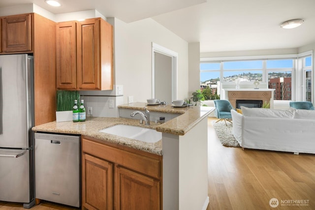 kitchen featuring a sink, light stone counters, a glass covered fireplace, stainless steel appliances, and light wood finished floors