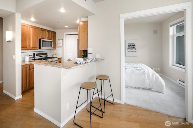 kitchen featuring light wood-style flooring, appliances with stainless steel finishes, a breakfast bar, and a baseboard radiator