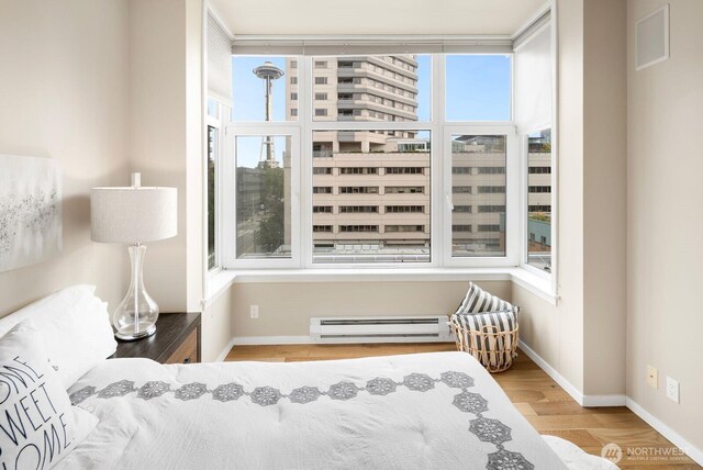 bedroom with a baseboard heating unit, multiple windows, wood finished floors, and baseboards