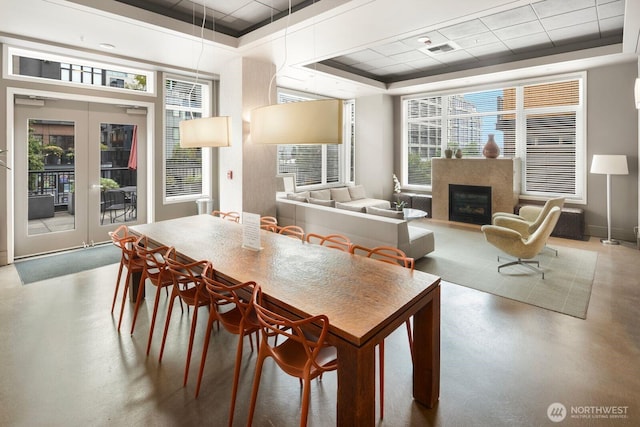 dining space with visible vents, a tray ceiling, finished concrete flooring, a high end fireplace, and french doors