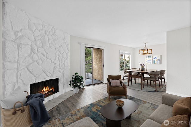 living area with an inviting chandelier, wood finished floors, baseboards, and a large fireplace