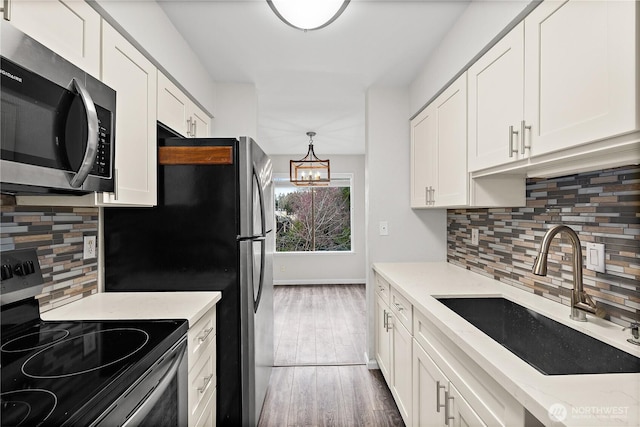 kitchen with wood finished floors, an inviting chandelier, a sink, stainless steel appliances, and white cabinets