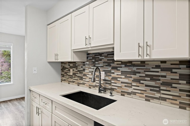 kitchen with backsplash, light stone counters, light wood-style floors, white cabinetry, and a sink