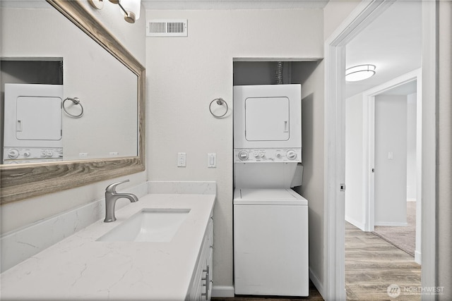 laundry area with visible vents, a sink, wood finished floors, stacked washer / dryer, and baseboards