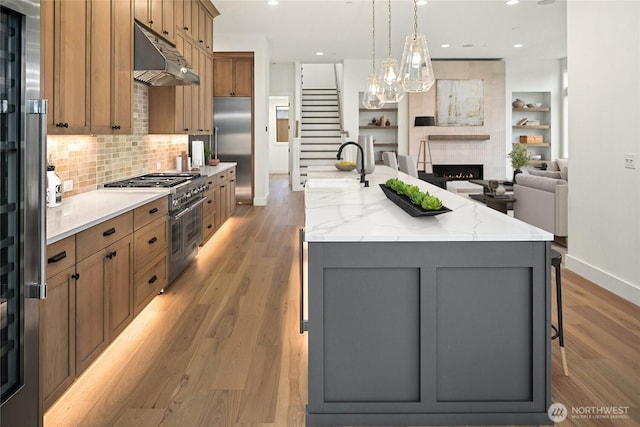 kitchen with under cabinet range hood, high end appliances, light wood-style flooring, and a large island with sink