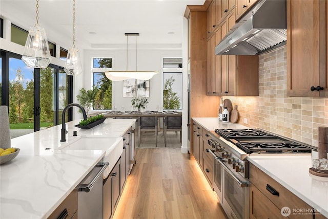 kitchen featuring backsplash, under cabinet range hood, light wood-style floors, brown cabinetry, and stainless steel appliances