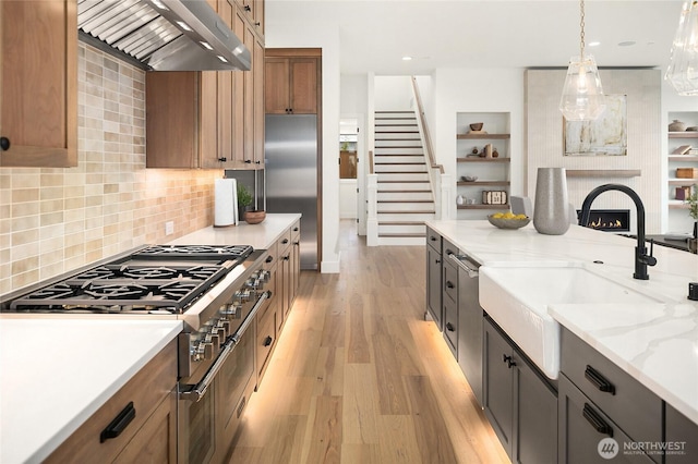 kitchen with a large fireplace, premium range hood, stainless steel built in refrigerator, light wood-style floors, and a sink