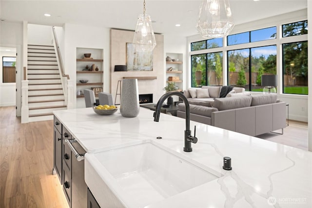 kitchen with built in shelves, decorative light fixtures, open floor plan, light wood-type flooring, and a sink