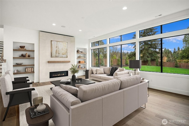 living room with a wealth of natural light, built in features, a large fireplace, and light wood-style floors