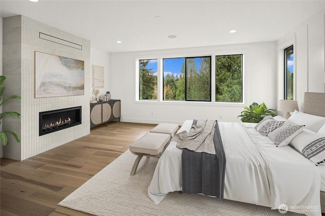 bedroom with recessed lighting, baseboards, wood finished floors, and a tiled fireplace