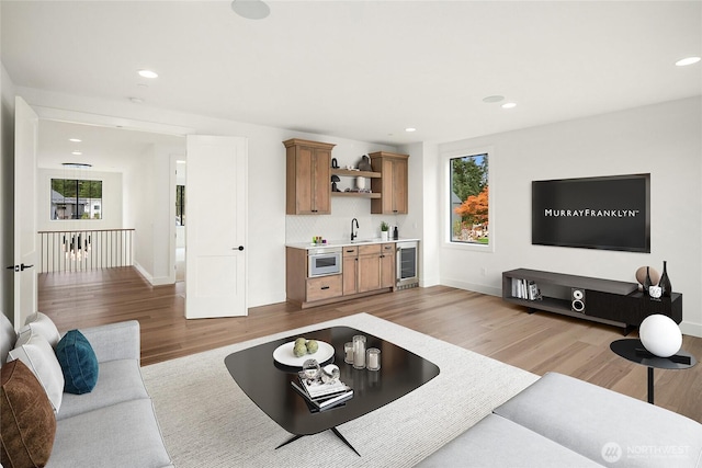 living room with baseboards, wine cooler, recessed lighting, light wood-style flooring, and wet bar