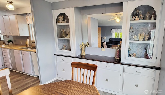 kitchen with a sink, dark countertops, wood finished floors, white cabinetry, and ceiling fan