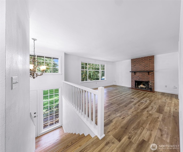 unfurnished living room with a fireplace, an inviting chandelier, wood finished floors, and baseboards