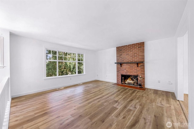 unfurnished living room with a brick fireplace, wood finished floors, and baseboards