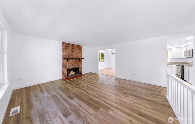 unfurnished living room featuring visible vents, baseboards, an inviting chandelier, a fireplace, and light wood-style floors