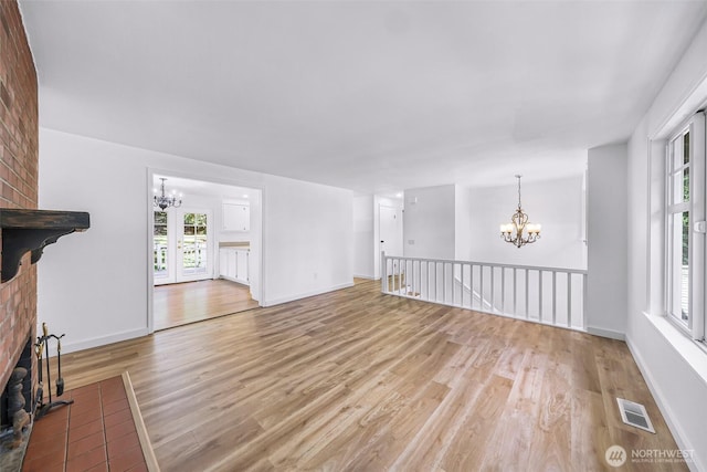 unfurnished living room featuring light wood-style floors, visible vents, a notable chandelier, and a fireplace