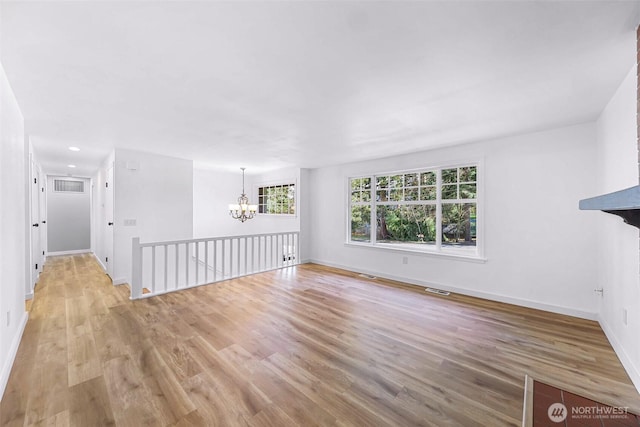 unfurnished living room featuring visible vents, a notable chandelier, wood finished floors, and baseboards