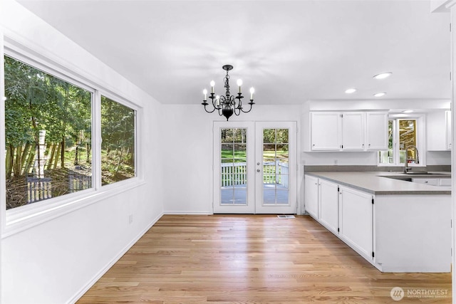 kitchen with light wood finished floors, baseboards, pendant lighting, a notable chandelier, and white cabinets