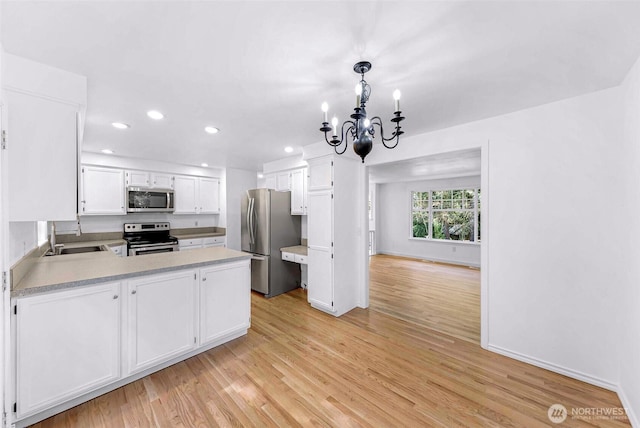 kitchen with a sink, light countertops, light wood-style floors, appliances with stainless steel finishes, and a notable chandelier