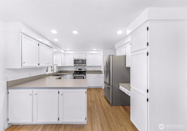 kitchen featuring light wood-type flooring, a sink, a peninsula, appliances with stainless steel finishes, and white cabinets